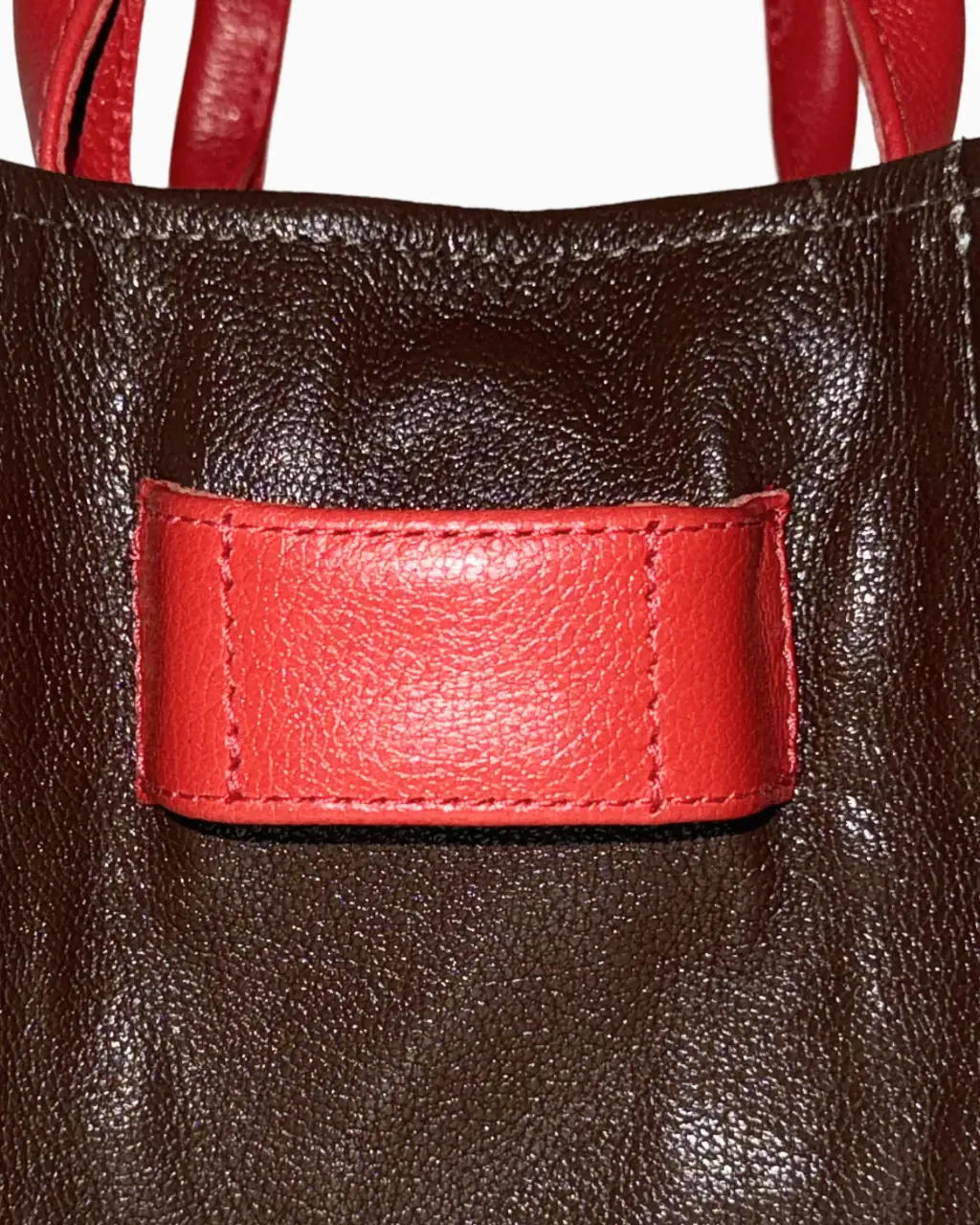 Detalhe do couro marrom da Core Tote Bag Agrado, com o bolso aplicado em couro vermelho costurado.