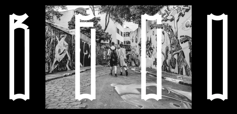 Letras altas e estreitas da Mosquito, em branco, ladeando uma fotografia em preto e branco de uma rua com grafites.